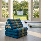 Blue Thai triangle floor mattress daybed, folded, in a garden yoga studio