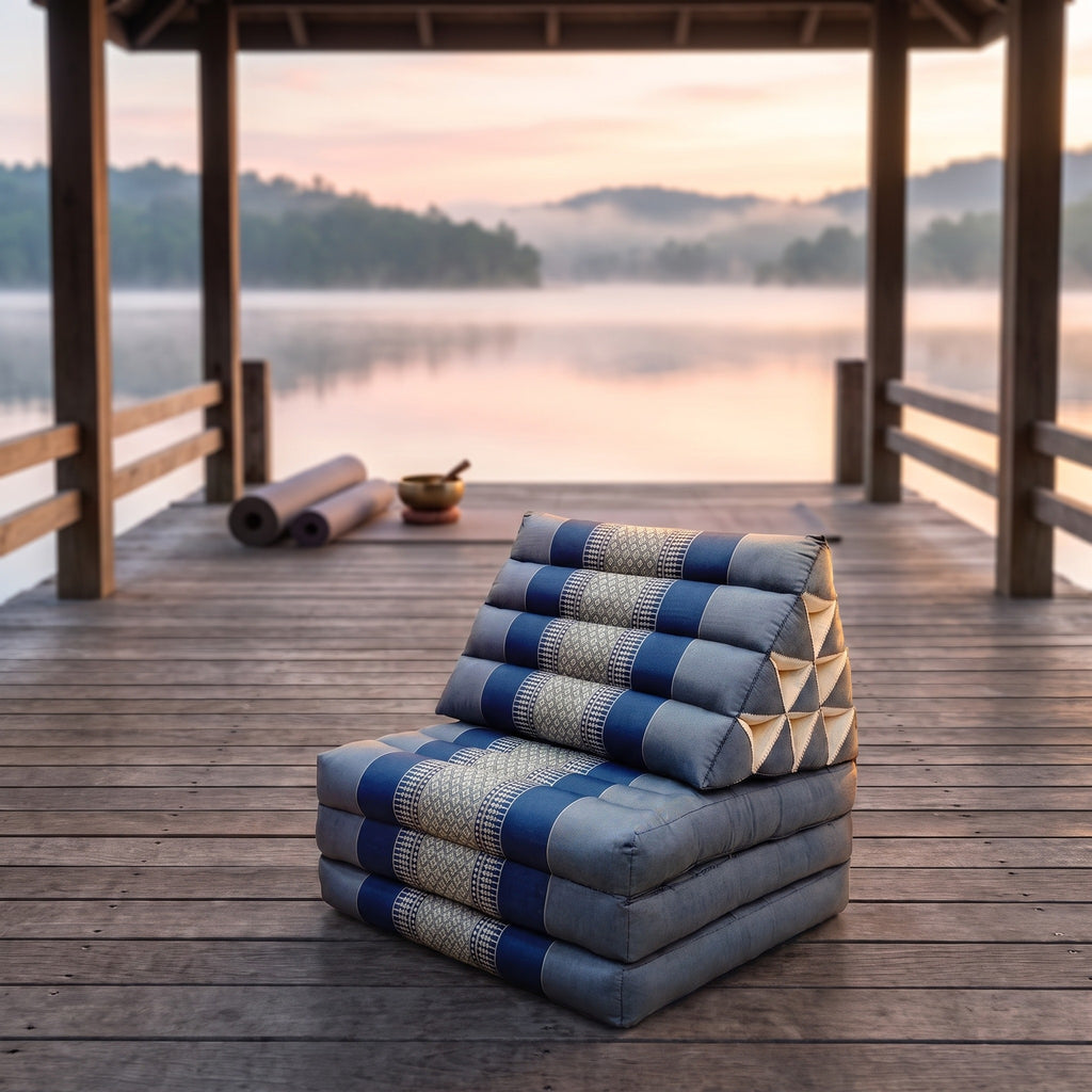 Grey-blue Thai triangle floor mattress daybed, folded, on a lakeside pavilion at dawn