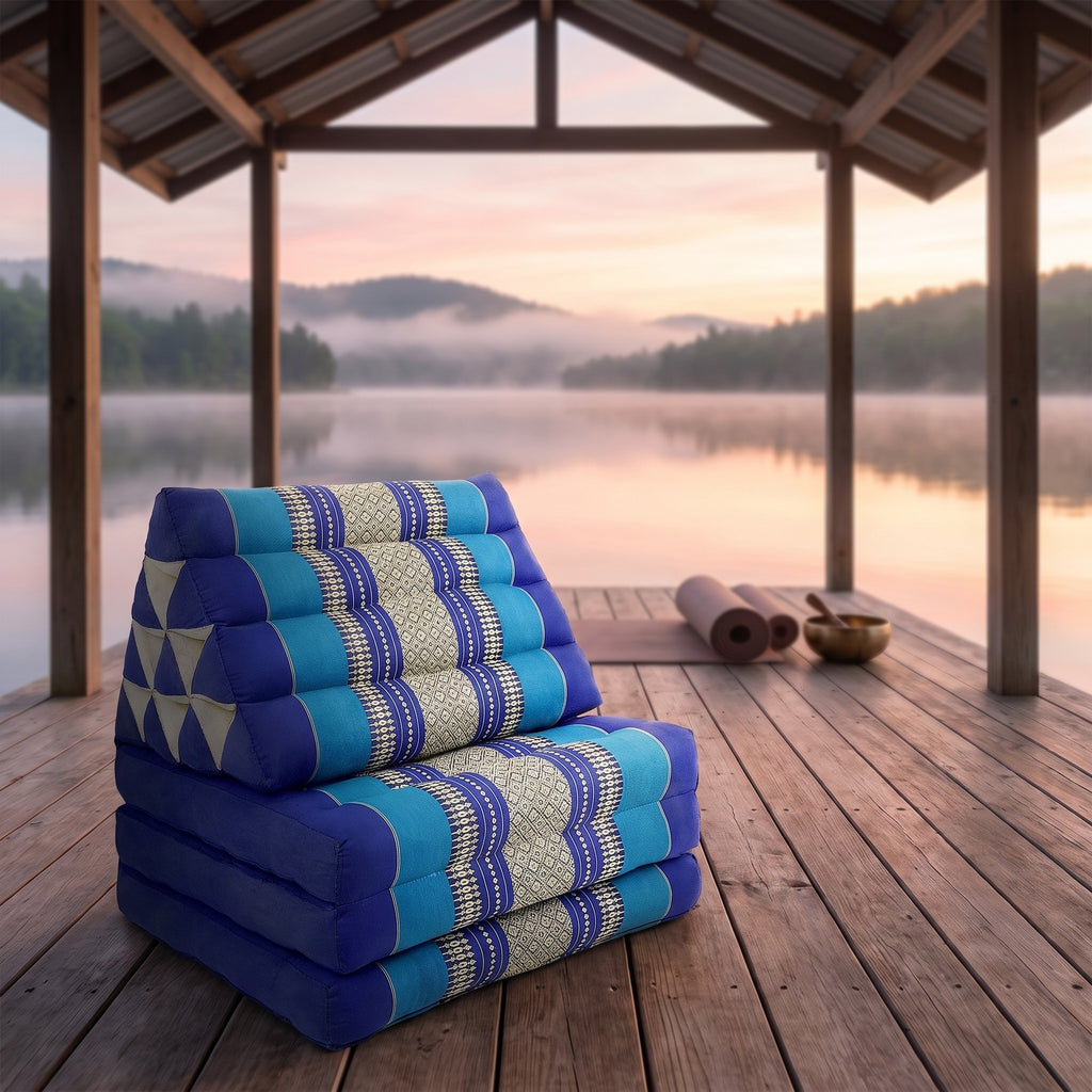 Navy Thai triangle floor mattress daybed, folded, on a lakeside pavilion at dawn