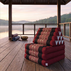 Red elephant pattern Thai triangle floor mattress daybed, folded, on a lakeside pavilion at dawn