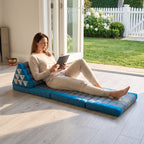 Woman reclining with a tablet on a blue Thai triangle floor mattress opened out as a lounger, in a garden sunroom