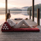 Woman reclining on a red Thai triangle floor mattress opened out as a lounger, on a lakeside pavilion at dawn