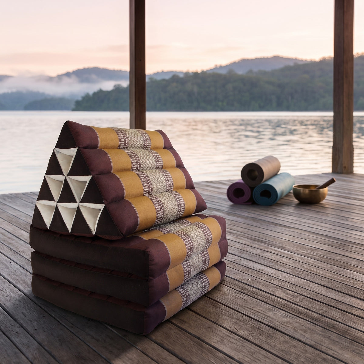 Brown Thai triangle floor mattress daybed, folded, on a lakeside pavilion at dawn