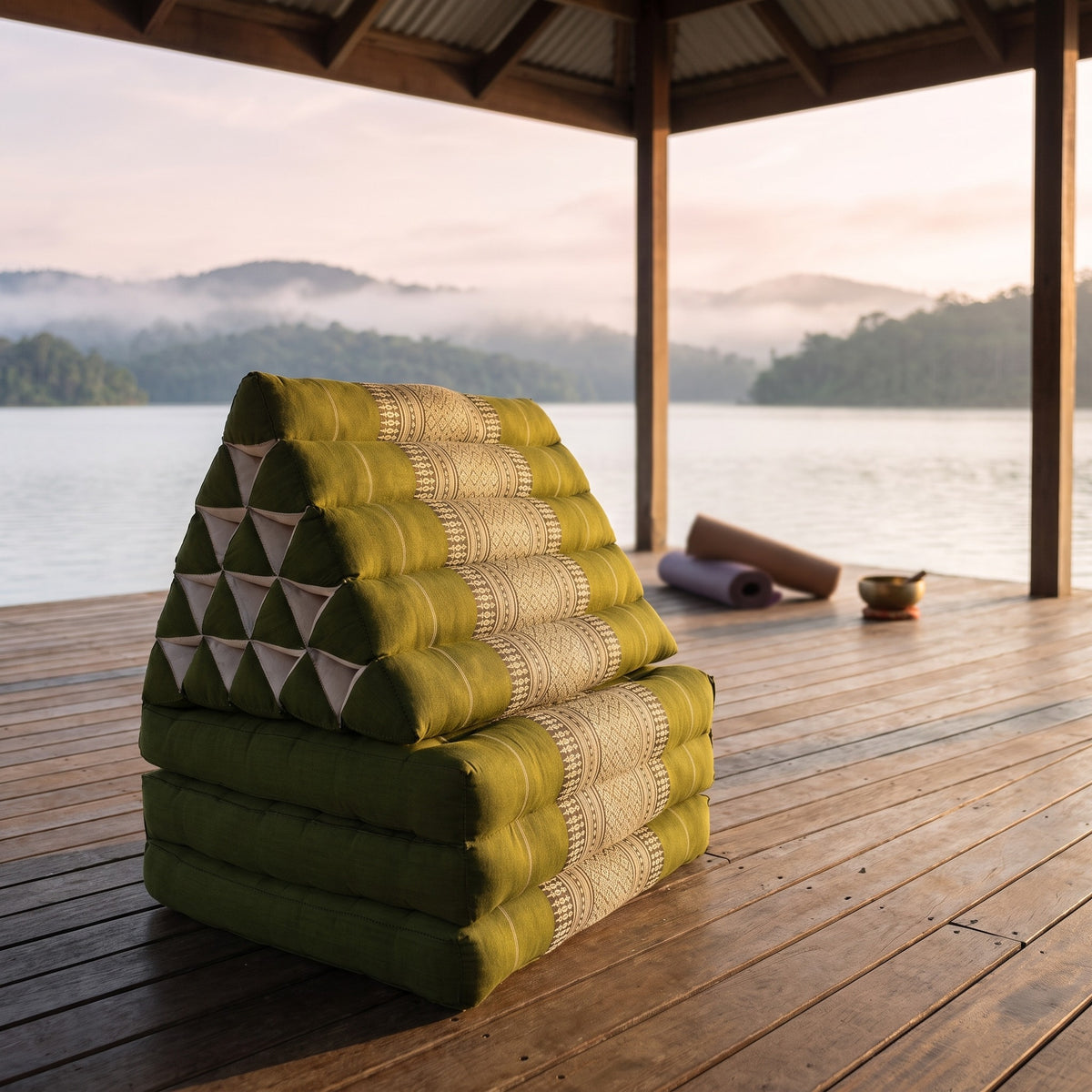 Green Jumbo 3-fold Thai triangle floor mattress, folded, on a lakeside pavilion at dawn