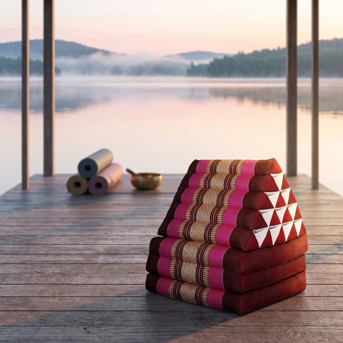Pink Jumbo 3-fold Thai triangle floor mattress, folded, on a lakeside pavilion at dawn