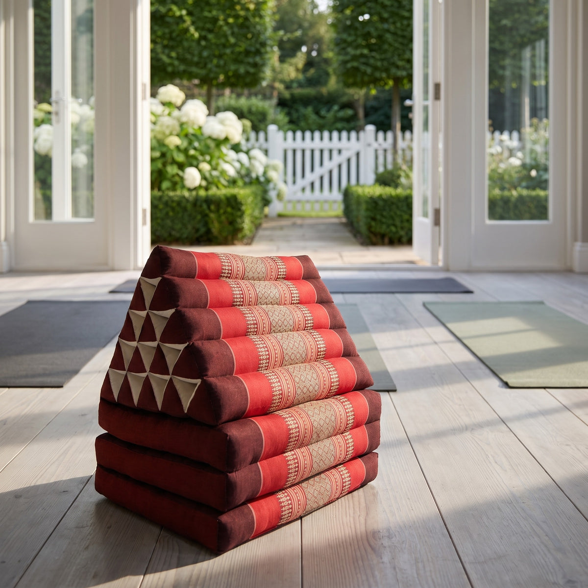 Red Jumbo 3-fold Thai triangle floor mattress, folded, in a garden yoga studio