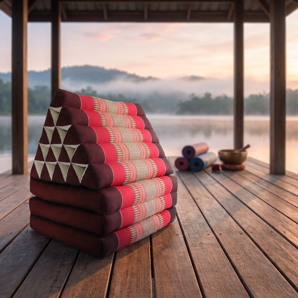 Red Jumbo 3-fold Thai triangle floor mattress, folded, on a lakeside pavilion at dawn