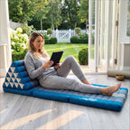 Woman reclining with a tablet on a blue Jumbo Thai triangle floor mattress opened out as a lounger, in a garden sunroom